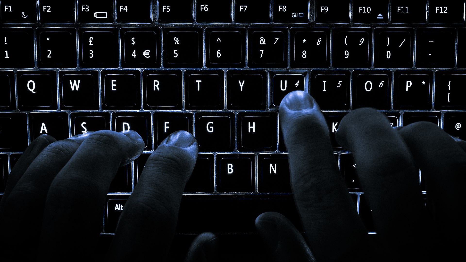A backlit laptop computer keyboard being used.